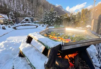 Чан на дровах зимой: вода с дольками цитрусов и хвоей, огонь под чаном, снег и горы